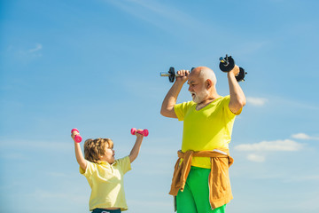 Sport exercise for kids. Boy is doing exercises to develop muscles. Grandfather helping kid...
