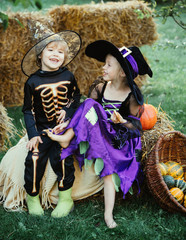 Trick-or-treating. Halloween Scene with cute children. Happy children with skeleton and witch costume holding and eating candies. Halloween sweets.