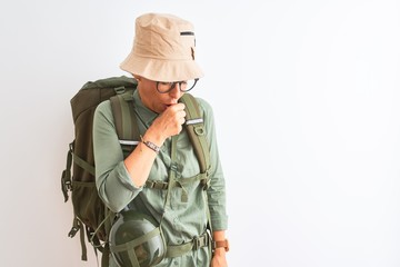 Middle age hiker woman wearing backpack canteen hat glasses over isolated white background feeling unwell and coughing as symptom for cold or bronchitis. Healthcare concept.