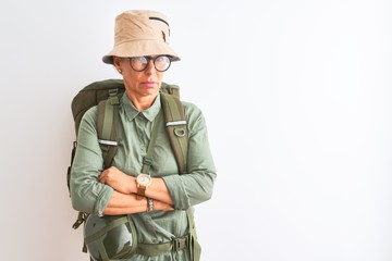 Fototapeta premium Middle age hiker woman wearing backpack canteen hat glasses over isolated white background skeptic and nervous, disapproving expression on face with crossed arms. Negative person.