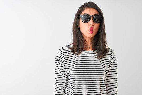 Chinese woman wearing striped t-shirt and sunglasses standing over isolated white background making fish face with lips, crazy and comical gesture. Funny expression.