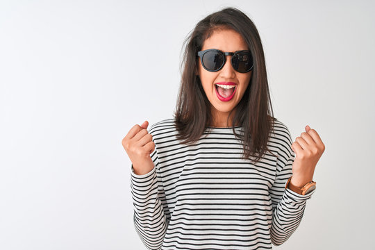 Chinese woman wearing striped t-shirt and sunglasses standing over isolated white background celebrating surprised and amazed for success with arms raised and open eyes. Winner concept.