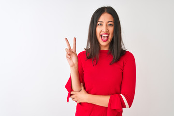 Young beautiful chinese woman wearing red dress standing over isolated white background smiling with happy face winking at the camera doing victory sign. Number two.