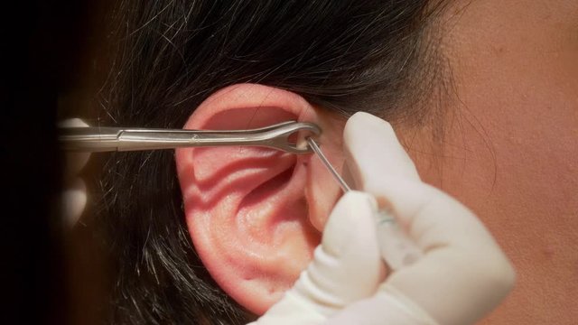 Woman gets pierced at the ear - piercing procedure in close up view