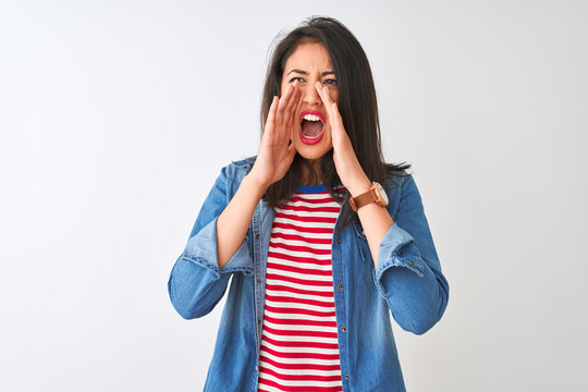 Young chinese woman wearing striped t-shirt and denim shirt over isolated white background Shouting angry out loud with hands over mouth