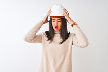Young chinese architect woman wearing security helmet over isolated white background suffering from headache desperate and stressed because pain and migraine. Hands on head.