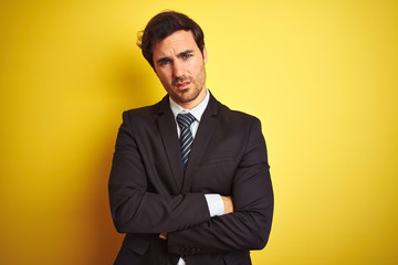 Young handsome businessman wearing suit and tie standing over isolated yellow background skeptic and nervous, disapproving expression on face with crossed arms. Negative person.