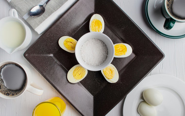 Obraz na płótnie Canvas Boiled eggs on a brown plate with coffee, cream and orange juice and salt