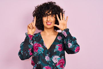 Young arab woman with curly hair wearing floral dress over isolated pink background showing and pointing up with fingers number six while smiling confident and happy.