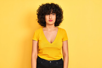 Young arab woman with curly hair wearing t-shirt standing over isolated yellow background skeptic and nervous, frowning upset because of problem. Negative person.