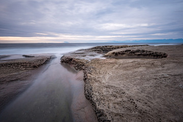 Fototapeta na wymiar rocky coast line filled with sand stone by the ocean under cloudy sky near dusk 