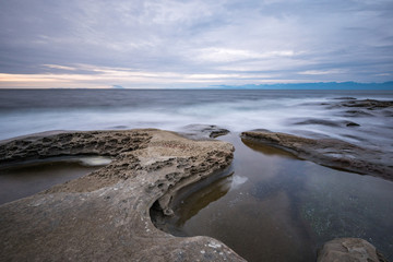 rocky coast line filled with sand stone by the ocean under cloudy sky near dusk 