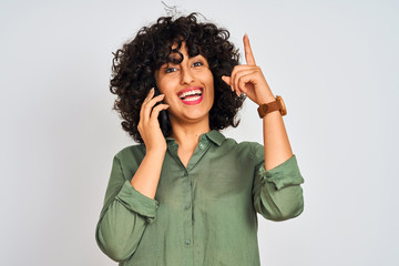 Young arab woman with curly hair talking on smartphone over isolated white background surprised with an idea or question pointing finger with happy face, number one