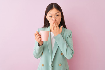 Young chinese businesswoman wearing glasses drinking coffee over isolated white background cover mouth with hand shocked with shame for mistake, expression of fear, scared in silence, secret concept