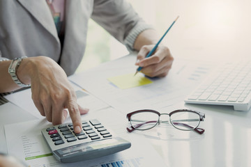 Close up Business woman using calculator and laptop for do math finance on wooden desk in office and business working background, tax, accounting, statistics and analytic research concept