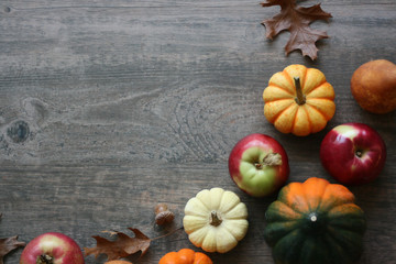 Fall harvest background with pumpkins, acorn squash, fruit and leaves border over dark wood table...