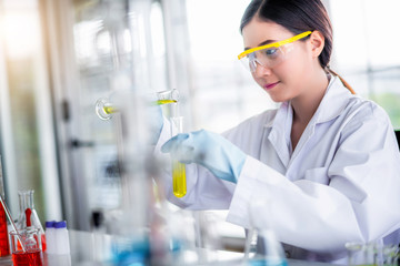 Attractive scientist woman looking chemical sample in flask at laboratory with lab glassware...