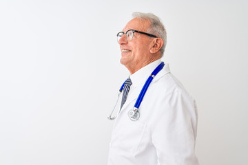 Senior grey-haired doctor man wearing stethoscope standing over isolated white background looking to side, relax profile pose with natural face with confident smile.