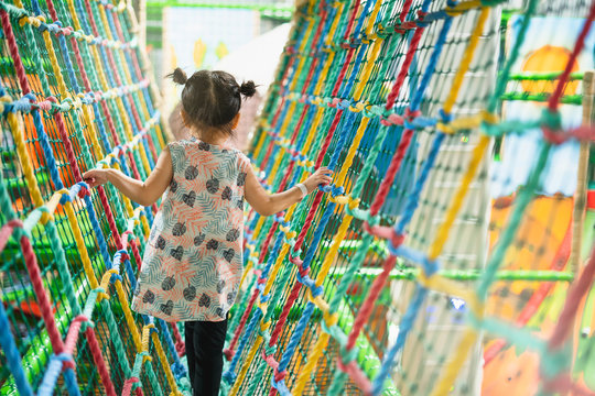 Little gile climbing the net. Happy kids on colorful ropes together in park. The girl on the playground. Little girl climbing in adventure park.