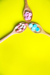 Top view Medicine on wood spoon.Assorted pharmaceutical red capsules with Multi color vitamins and supplements.They are on Yellow background and copy space.Photo concept healthy and medication.