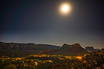 Moon rising at Airport Mesa vortex over Sedona city lights at night with red sandstone buttes