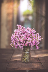 A bouquet of purple flowers in a glass vase on a wooden floor boards of old vintage.