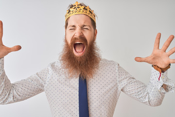 Young redhead irish businessman wearing crown king over isolated white background celebrating mad...