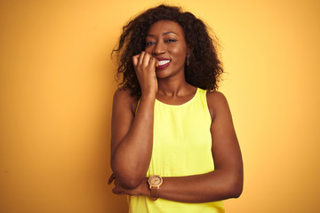 Young african american woman wearing t-shirt standing over isolated yellow background looking stressed and nervous with hands on mouth biting nails. Anxiety problem.