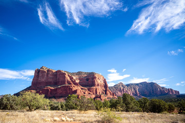 Wide Angle of Courthouse Butte red sandstone sedimentary rock formation in Sedona AZ under bright blue sky with wispy clouds
