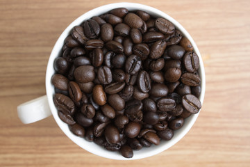 Coffee beans in a white mug on an old brown wood texture background