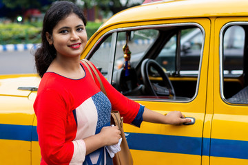 Young Indian woman opening gate of old yellow taxi 