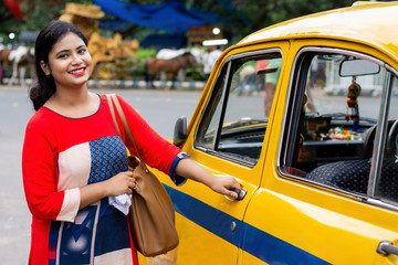 Young Indian woman opening gate of old yellow taxi 