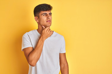 Obraz premium Young indian man wearing white t-shirt standing over isolated yellow background Touching painful neck, sore throat for flu, clod and infection