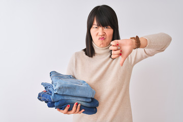 Beautiful Chinese shopkeeper woman holding folded jeans over isolated white background with angry...