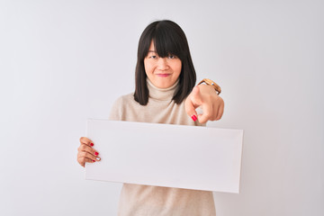 Young beautiful Chinese woman holding banner standing over isolated white background pointing with finger to the camera and to you, hand sign, positive and confident gesture from the front