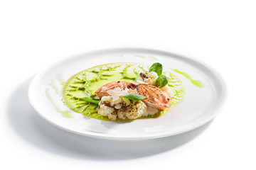 Salmon steak on plate closeup. Red fish piece with green pea puree and cauliflower. Salmon with creamy sauce and vegetables isolated on white background. Restaurant tasty dish, cooked healthy meal
