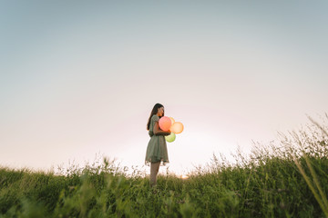 Tone film of lonely asian woman holding colorful balloons on green field with sunset time