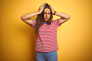 Young beautiful woman wearing striped t-shirt standing over isolated yellow background suffering from headache desperate and stressed because pain and migraine. Hands on head.