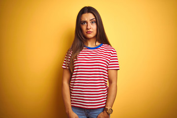 Young beautiful woman wearing striped t-shirt standing over isolated yellow background skeptic and nervous, frowning upset because of problem. Negative person.