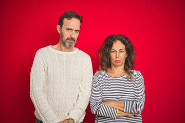 Beautiful middle age couple wearing winter sweater over isolated red background skeptic and nervous, frowning upset because of problem. Negative person.