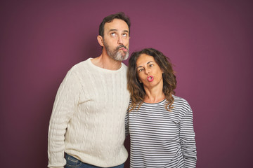 Beautiful middle age couple wearing winter sweater over isolated purple background making fish face with lips, crazy and comical gesture. Funny expression.