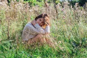 Happy young beautiful woman in sweater and underpants sitting with bare foot in a field of dry agrimony