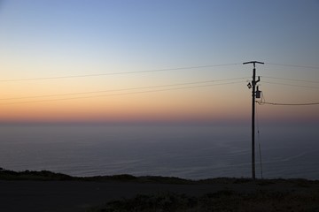 Wire pole on the hill with the sea and a blue sky at sunset