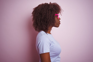 Young african afro woman wearing t-shirt glasses over isolated pink background looking to side, relax profile pose with natural face with confident smile.