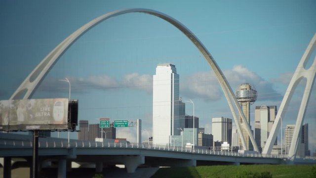 The Dallas Skyline is Framed by the Margaret McDermott Bridge with the Iconic Reunion Tower in the center. Slow moving traffic drives over the bridge on a beautiful day. - 4K version