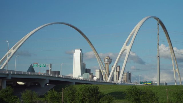 4K - The Dallas Skyline is Framed by the 2 Arches of the Margaret McDermott Bridge with the Iconic Reunion Tower in the center. Slow moving traffic drives over the bridge on a beautiful day.