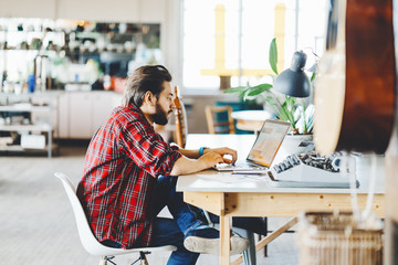 Man with stubble and flannel shirt working with laptop in spacious office space