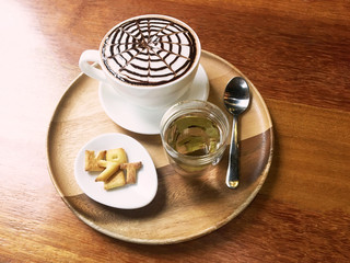 Hot Cappuccino or Latte coffee  topped with chocolate sauce with Tea and Biscuit on wooden plate, on wooden table background in cafe.