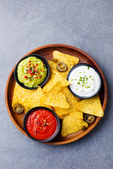 Nachos chips in bowl with sauces, dip variety. Grey stone background. Top view.