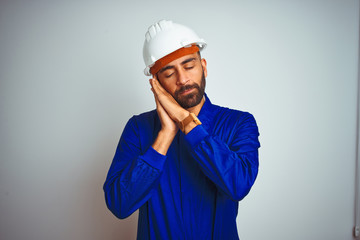 Handsome indian worker man wearing uniform and helmet over isolated white background sleeping tired dreaming and posing with hands together while smiling with closed eyes.